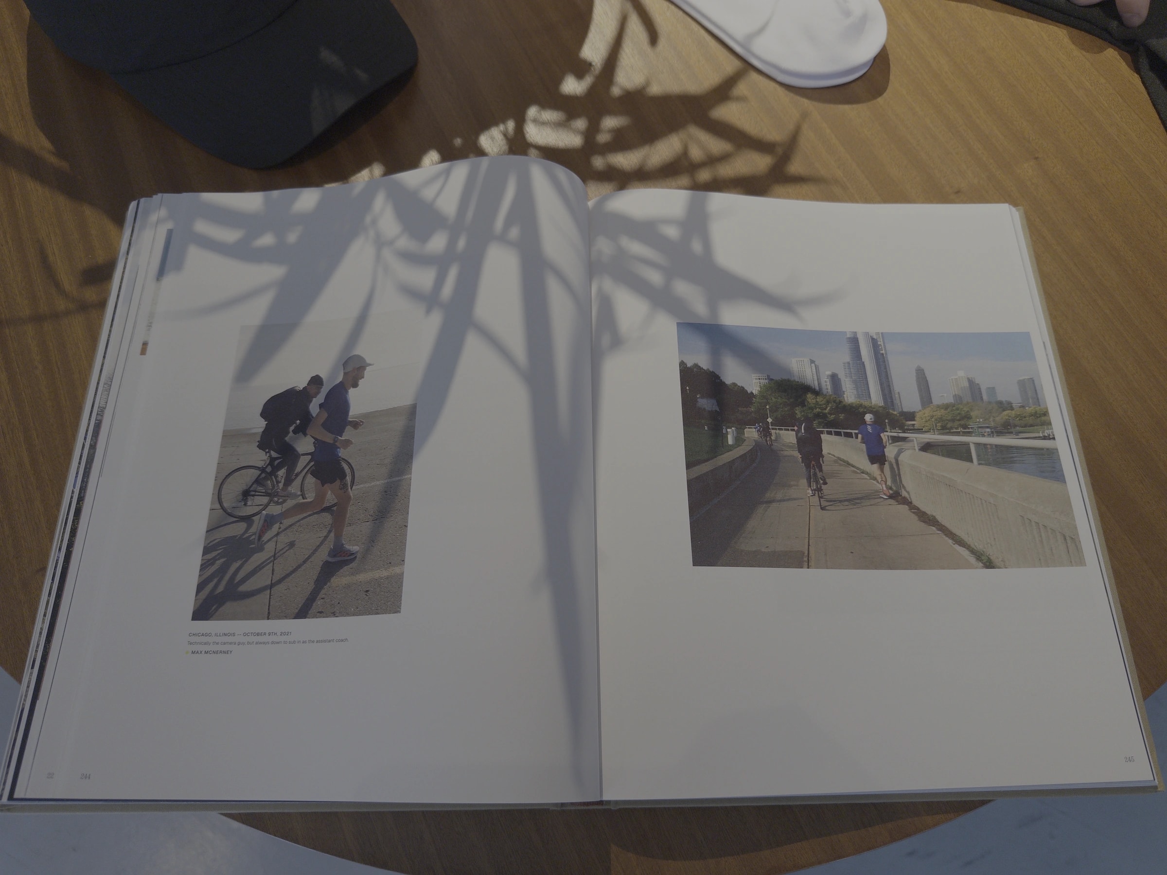 An open running photography book on a wooden table, with sunlight and leaf shadows across its pages.